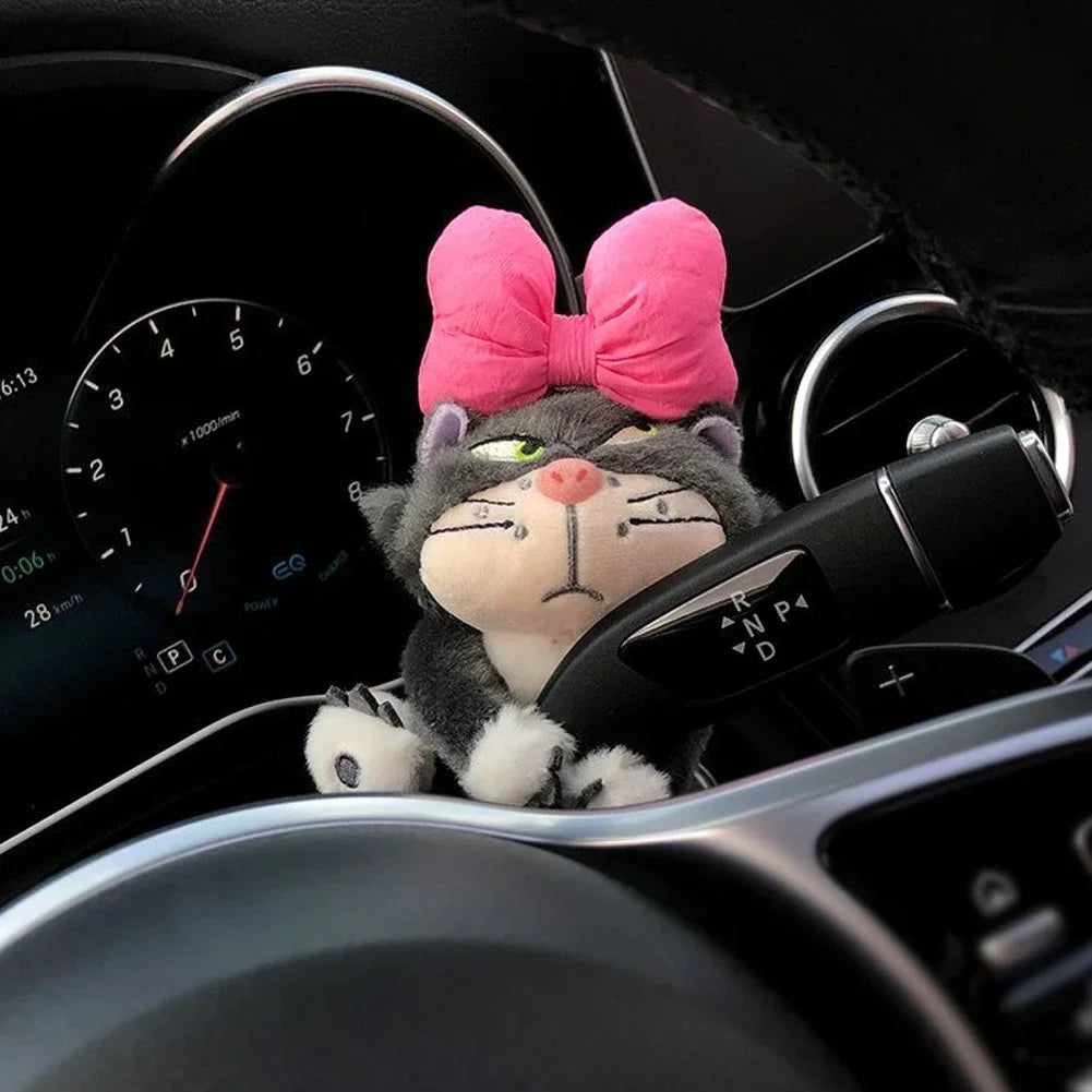 Cat plush toy with pink bow clipped onto car gear shifter as a cute dashboard accessory