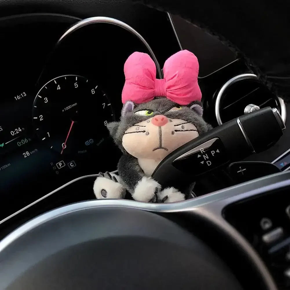 Grumpy cat plush toy with pink bow clipped to luxury car gear stalk on dashboard