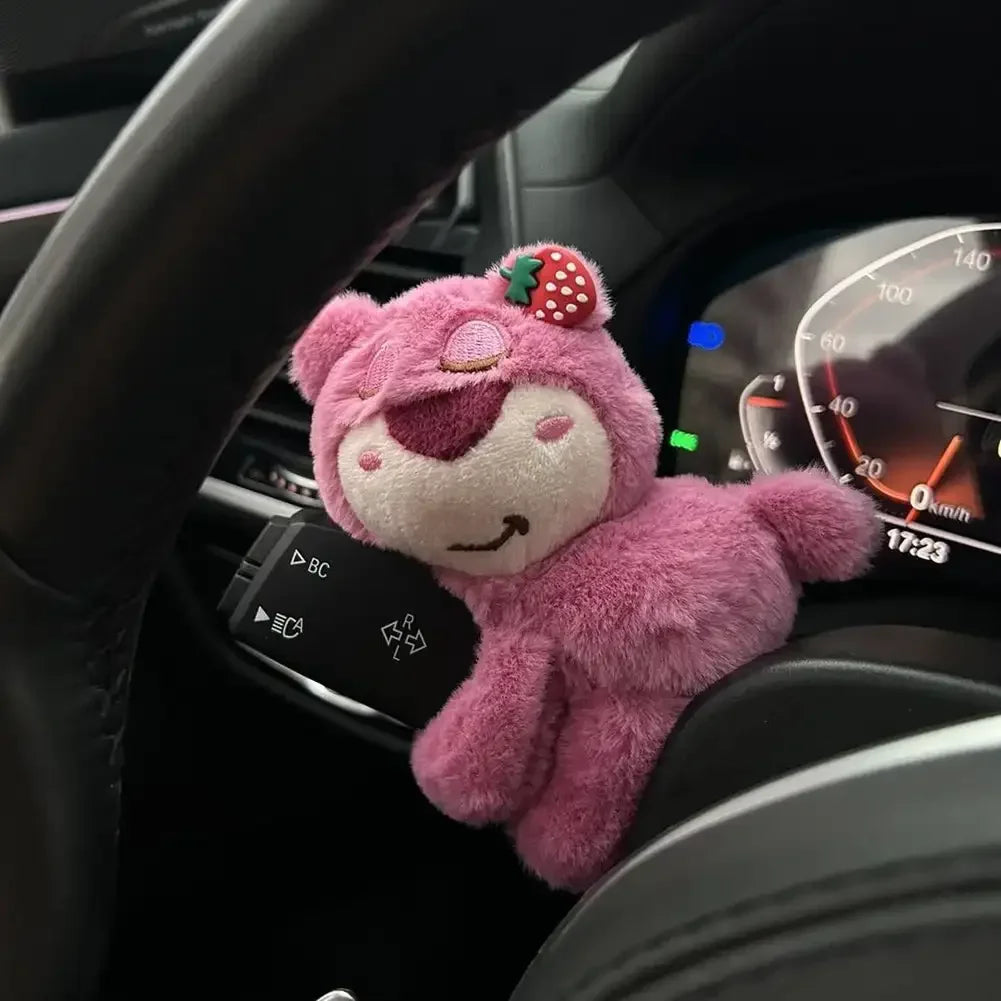 Pink bear plush toy clipped to car dashboard near steering wheel and speedometer