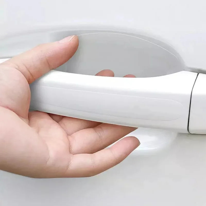 Hand gripping white car door handle with clear PVC scratch guard film installed in bowl