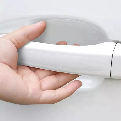 Hand gripping white car door handle with clear PVC scratch guard film installed in bowl