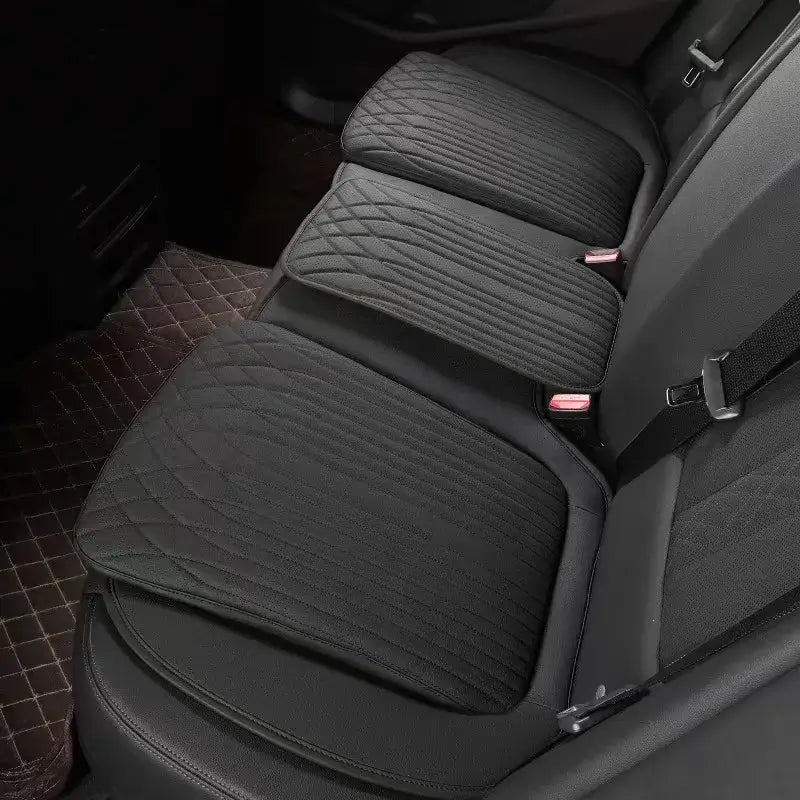 Black leather car seat height cushion installed on rear seat showing thick padded profile and perforated surface
