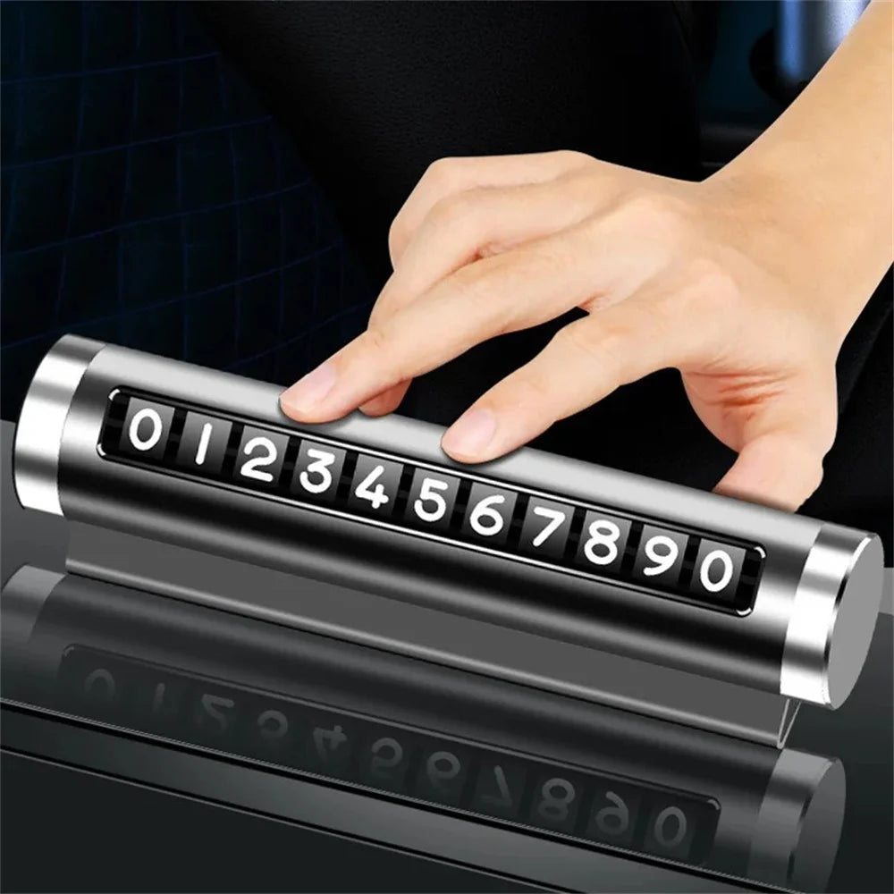 Black metal parking number plate lying flat with 0 to 9 digits displayed and hand pressing number roller from above