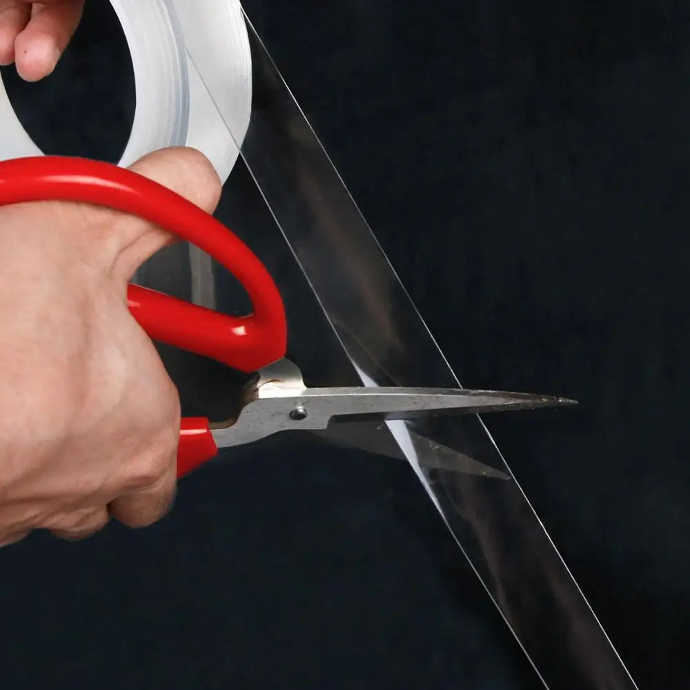 Transparent car door sill protection film being cut with red-handled scissors before application
