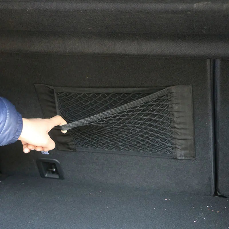 Hand pulling adjustment strap on trunk cargo net mounted on car boot side wall