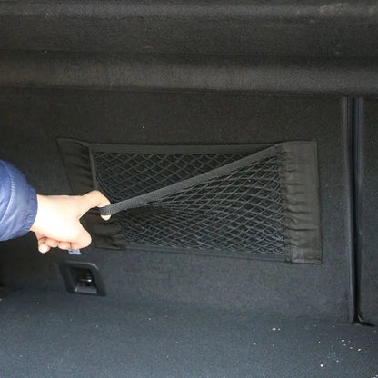 Hand pulling adjustment strap on trunk cargo net mounted on car boot side wall