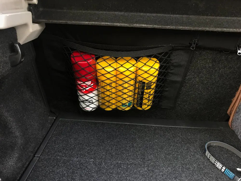 Trunk cargo net installed under car boot lid holding spray bottles and car care products